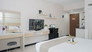 Quarto de hotel com uma cama, uma escrivaninha com cadeira, televisão, máquina de café e uma porta.