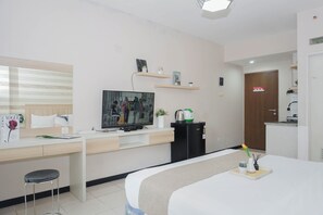 Quarto de hotel com uma cama, uma escrivaninha com cadeira, televisão, máquina de café e uma porta.