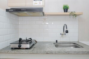 A kitchen with a gas stove, a sink, a stainless steel range hood, and a potted plant on a shelf. - Best Price Studio At Bogor Valley Apartment (Bogor)