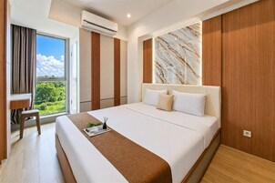 A modern hotel room with a large bed, a desk, and a view of greenery.