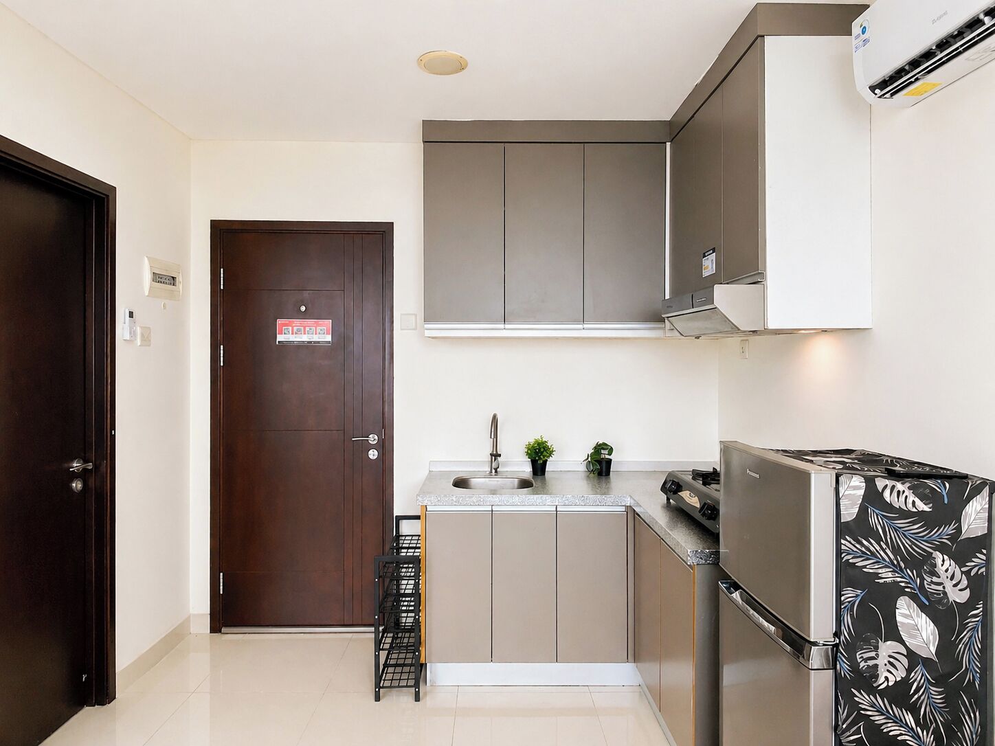A compact kitchen with a dark wooden door, a stainless steel refrigerator, and a built-in oven.