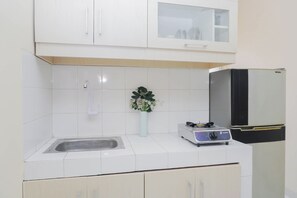 A kitchen with white cabinets, a sink, a vase with flowers, and a gas stove. - Good Deal And Homey 1Br Apartment At Cibubur Village (Depok)