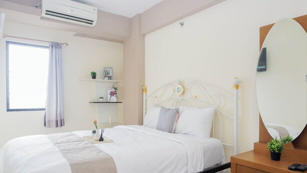 Habitación de hotel con cama, mesita de noche, lámpara de noche, equipo de aire acondicionado, ventana con cortinas y espejo montado en la pared.
