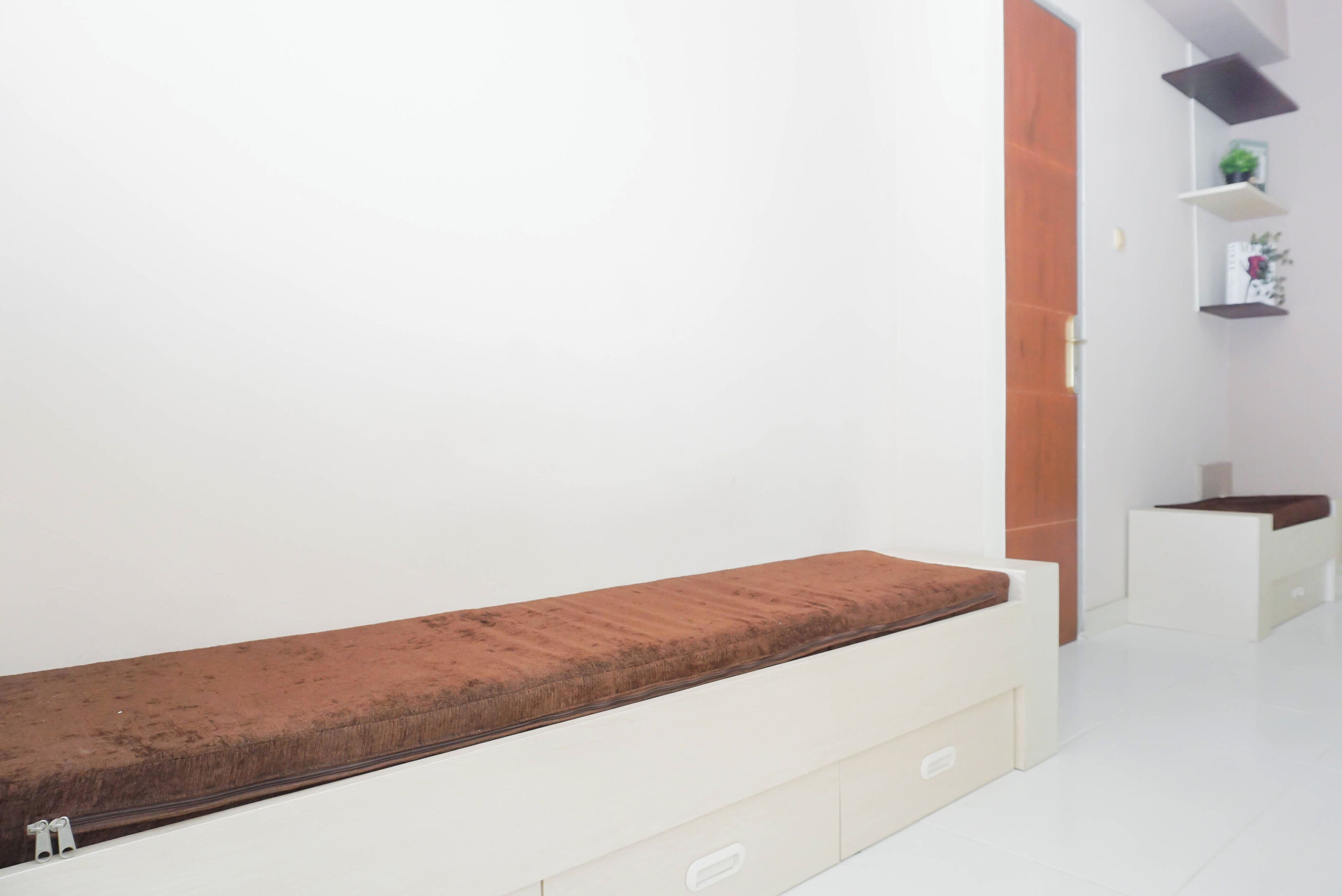 Una habitación minimalista con una banca, una puerta de madera y una pared blanca con estantes.