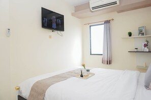 Ein Hotelzimmer mit einem Bett, einem Wand-Fernseher, einem Fenster mit Vorhängen, einem Nachttisch mit Pflanze und einem Regal mit Büchern und einer Vase.