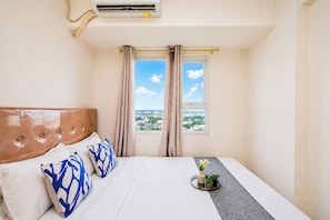 Ein Hotelzimmer mit Bett, Vorhängen, einer Klimaanlage und einem Fenster mit Blick auf die Stadt.