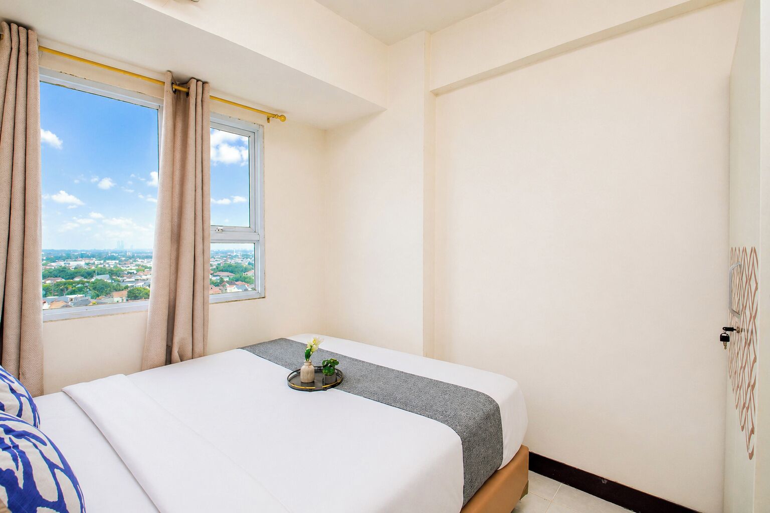 Un dormitorio con cama, ventana con cortinas, vista de la ciudad y una puerta con cerradura.