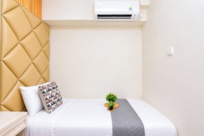 Ein Hotelzimmer mit Bett, Kopfteil, Klimaanlage, einer kleinen Pflanze und einem Nachttisch.