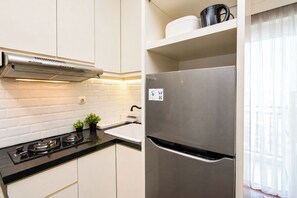 Eine moderne Küche mit weißen Schränken, einem Edelstahlherd, einem Kühlschrank und einem Fenster mit transparenten Vorhängen.