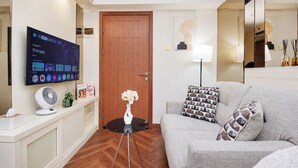A modern living room with a flat-screen TV, a sofa, a small side table, a lamp, and a wooden door. - Neat And Homey 2Br Apartment Cinere Resort (Depok)