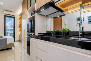 Una cocina moderna con encimera negra, pileta de acero inoxidable y campana extractora. Hay alacenas y un ventanal con vista a edificios.