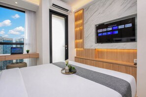 Una habitación de hotel moderna con una cama, un televisor montado en la pared, un ordenador portátil sobre un escritorio y vistas a la ciudad.