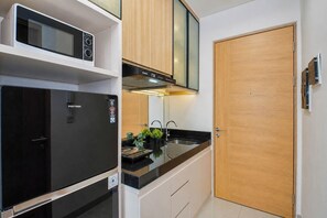 Una cocina compacta con un refrigerador negro, un microondas, un lavavajillas y una puerta de madera.