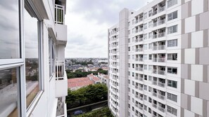 A high-rise building with multiple balconies, a view of the cityscape, and a red-tiled roof visible through the windows. - 1 Pax Wooden Touch Studio At Citra Living Apartment (Jakarta)