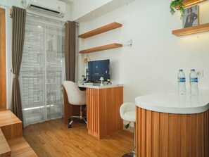 A modern office space with a desk, computer, chair, and a reception area with a counter and water bottles. - 1 Pax Wooden Touch Studio At Citra Living Apartment (Jakarta)