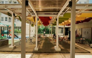 An indoor patio area with tables and chairs, a playground in the background, and a view of the building's exterior. - 1 Pax Wooden Touch Studio At Citra Living Apartment (Jakarta)