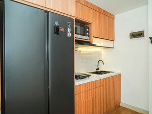 A kitchen with a stainless steel refrigerator, a microwave, a sink, and wooden cabinetry. - 1 Pax Wooden Touch Studio At Citra Living Apartment (Jakarta)
