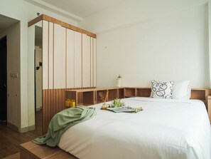 A modern bedroom with a large bed, wooden headboard, bedside tables, a green throw blanket, and a small plant. - 1 Pax Wooden Touch Studio At Citra Living Apartment (Jakarta)