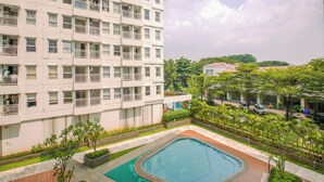 A high-rise building with multiple balconies, a swimming pool, and surrounding greenery. - Homey And Neat Studio Room At Apartment Citra Living (Jakarta)