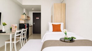 A hotel room with a bed, a desk with a chair, a small kitchen area, and a door. - Homey And Neat Studio Room At Apartment Citra Living (Jakarta)