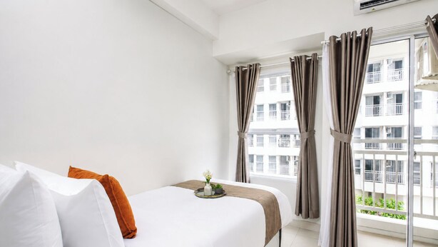A hotel room with a bed, a window with curtains, and a view of buildings. - Homey And Neat Studio Room At Apartment Citra Living (Jakarta)