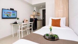 Habitación de hotel con cama, escritorio con sillas, televisor, refrigerador y una pequeña cocina.