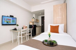 Ein Hotelzimmer mit Bett, Schreibtisch mit Stühlen, Fernseher, Kühlschrank und einer kleinen Küchenzeile.