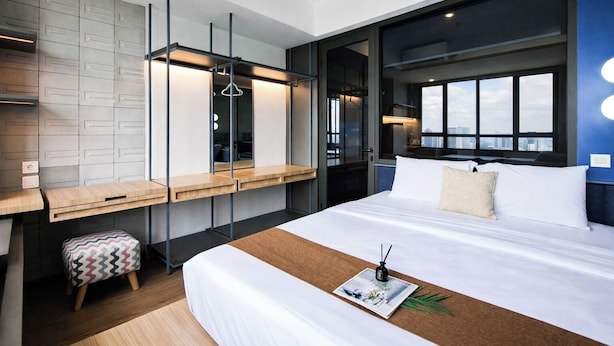 A modern hotel room with a large bed, a desk, and a view of the city. - Stylish 1Br At Collins Boulevard Apartment (Tangerang)