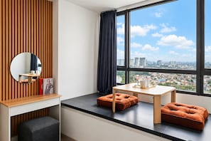 Une chambre moderne avec une grande fenêtre, un miroir rond, un bureau en bois et deux coussins orange.