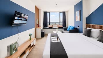 Habitación de hotel con cama, mesita de noche, televisor, ventana y vista a la ciudad.
