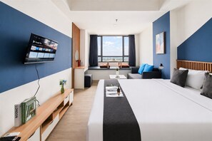 A hotel room with a bed, bedside table, TV, window, and a view of the city. - Relaxing With Chic Design Studio Apartment At Collins Boulevard (Tangerang)