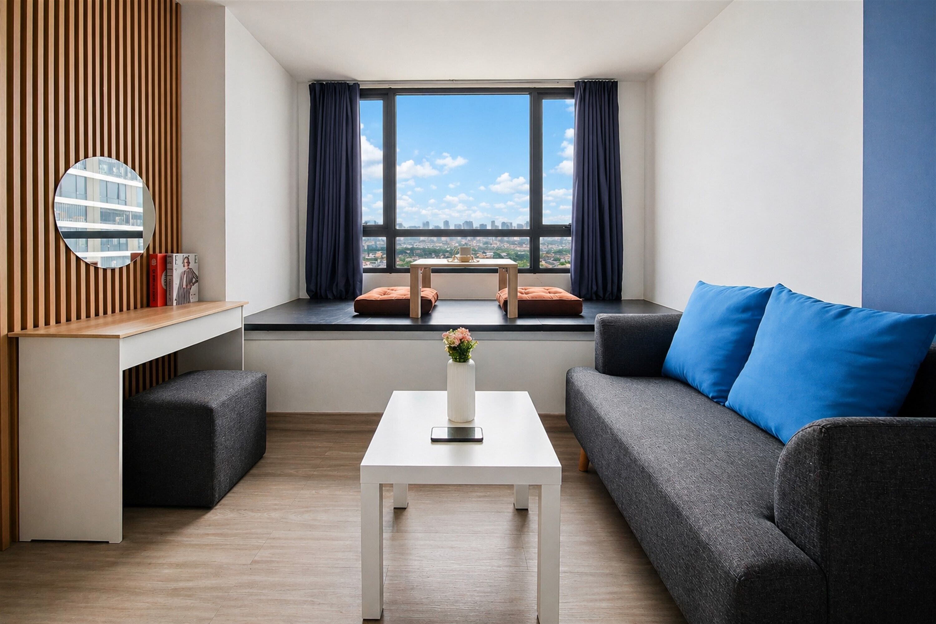 A modern living room with a sofa, a coffee table, a small table with a vase, and a view of the city through large windows.