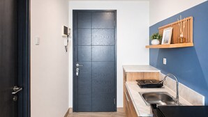 Cozinha compacta com porta escura, prateleira de madeira com uma planta, pia e bancada.