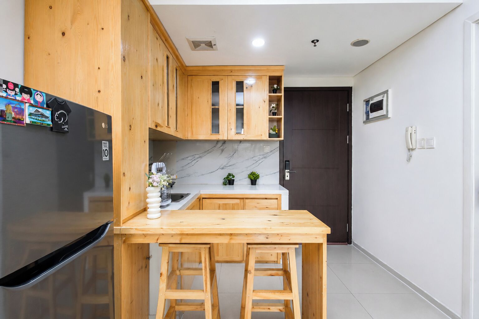 A kitchen with wooden cabinets, a marble countertop, a black refrigerator, and a small island with stools.