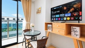 Een moderne kamer met een grote televisie waarop een film draait, een eethoek met een tafel en stoelen, en een stadszicht door een groot raam.