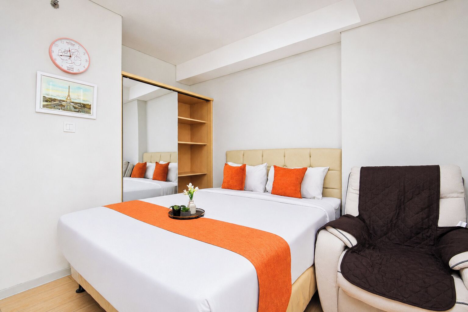 Une chambre d’hôtel avec un lit, une chaise, un miroir et une horloge au mur.