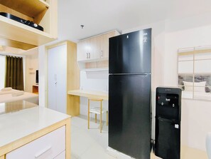 A compact kitchen with a black refrigerator, a small dining table, and a white countertop. - 2 Pax Neat Studio At De Prima Apartment (Medan)