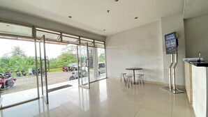 A spacious lobby with a glass door leading outside, a reception desk, and a small table with chairs. - Neat Studio With Blue Toned Wall At Dramaga Tower Apartment (Dramaga)