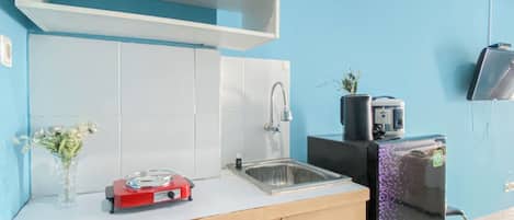 Een keuken met een gootsteen, een rode inrichting, een kleine plant en een televisie aan de muur.