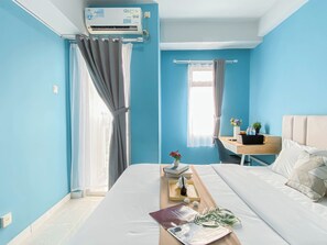 Ein Hotelzimmer mit Bett, Schreibtisch, Stuhl, Klimaanlage und einem fensterbepflanzten Fenster.