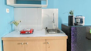 A kitchen with a sink, a red appliance, a potted plant, and a rice cooker. - Neat Studio With Blue Toned Wall At Dramaga Tower Apartment (Dramaga)