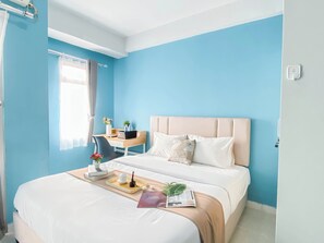 A hotel room with a bed, a desk, and a window. - Neat Studio With Blue Toned Wall At Dramaga Tower Apartment (Dramaga)