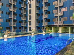 A modern building with a blue exterior and a pool area. - Good Location Studio Apartment At Evenciio Margonda (Depok)