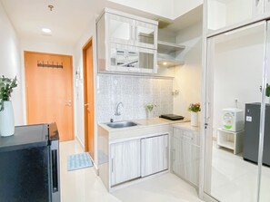 A modern kitchen with white cabinets, a stainless steel sink, a microwave, and a refrigerator. - Good Location Studio Apartment At Evenciio Margonda (Depok)