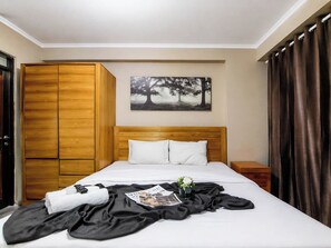 A hotel room with a bed, wooden wardrobe, a painting of trees, a nightstand, and a window with curtains. - Compact 2 Pax Studio Room At Gateway Pasteur Apartment (Cimahi)