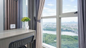 A room with a large window, a chair, a desk, and a vase with flowers. - 1Br Homey Areum Residence At Gold Coast (Jakarta)