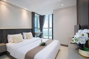 A modern hotel room with a large bed, a desk, and a view of the city. - 1Br Homey Areum Residence At Gold Coast (Jakarta)