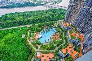 A high-rise building with a rooftop pool surrounded by greenery and a river in the background. - 1Br Homey Areum Residence At Gold Coast (Jakarta)