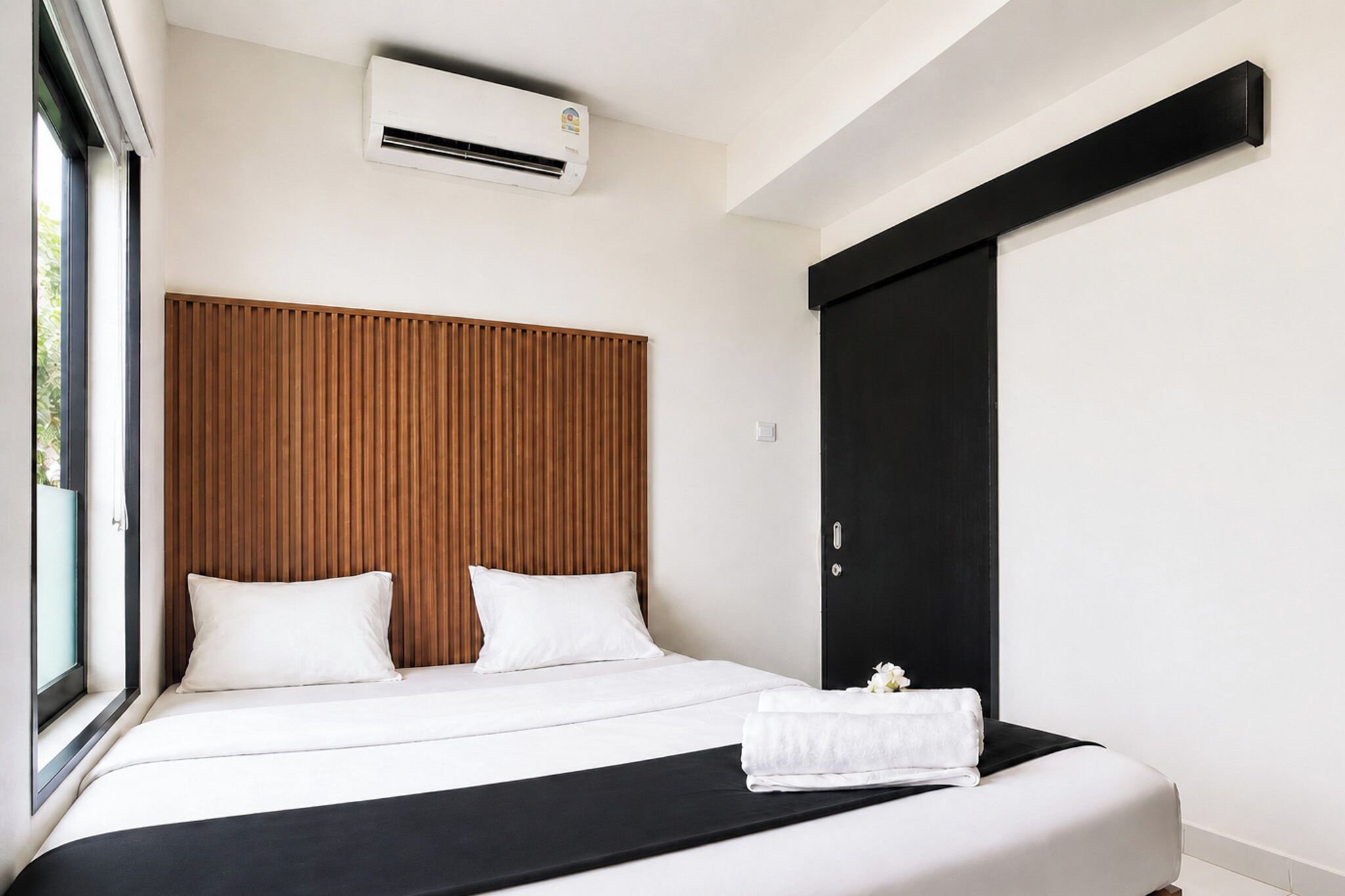 Une chambre d’hôtel moderne avec un grand lit, une fenêtre, un appareil de climatisation et une armoire noire.