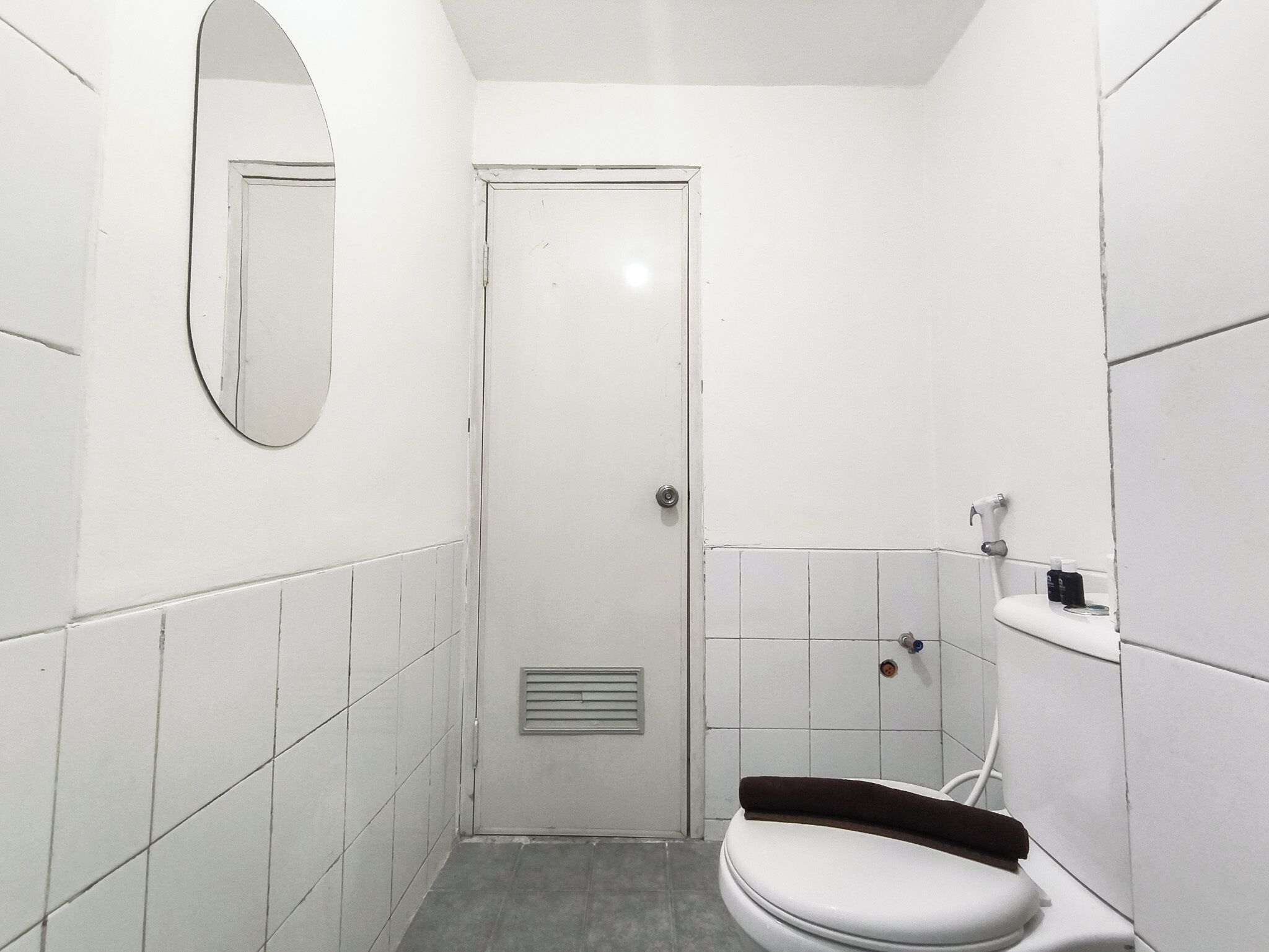 Une petite salle de bain blanche, avec des toilettes, un miroir et une porte.